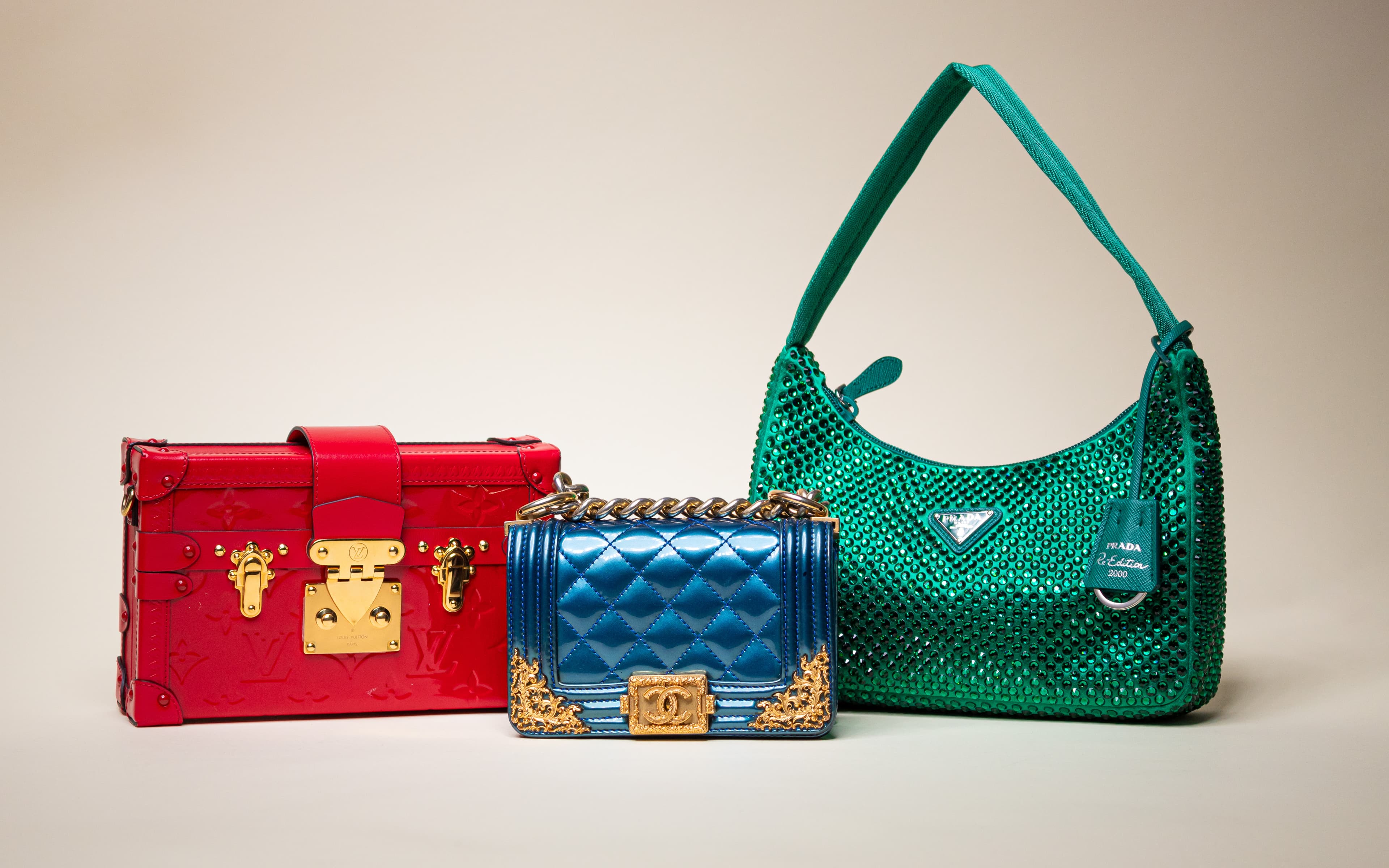 Three luxury handbags: red rectangular with gold hardware, small blue quilted purse with gold details.